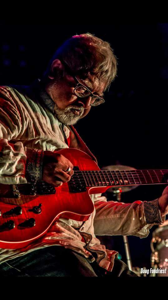 Fareed Haque playing a red electric guitar.